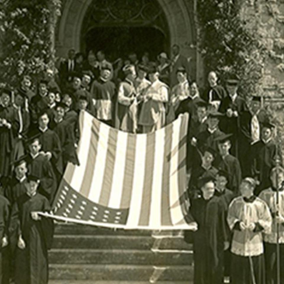 St. Edward's students and Holy Cross Brothers stand in front of the school with an American flag in the 1920s